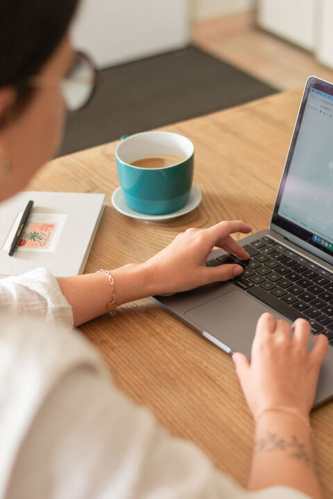 Person working on laptop at wood table with notebook and coffee cup.