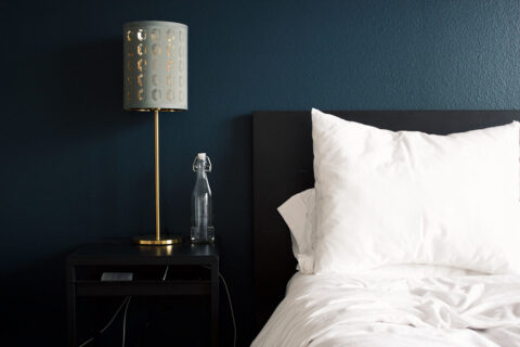 Bedroom with deep blue accent wall, plush bed with clean white bedding, and bedside table with lamp and water bottle.