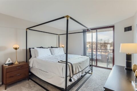 Bedroom with plush carpet, four post bed, bedside tables with lamps, and sliding balcony door.