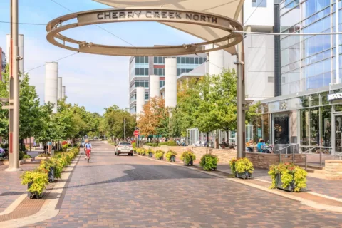 Fillmore Plaza with brick paved intersection, large Cherry Creek North sign, lush landscaping, and bustling restaurants.