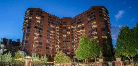 Seasons of Cherry Creek apartments with towering brick building and warm bright pool beneath.